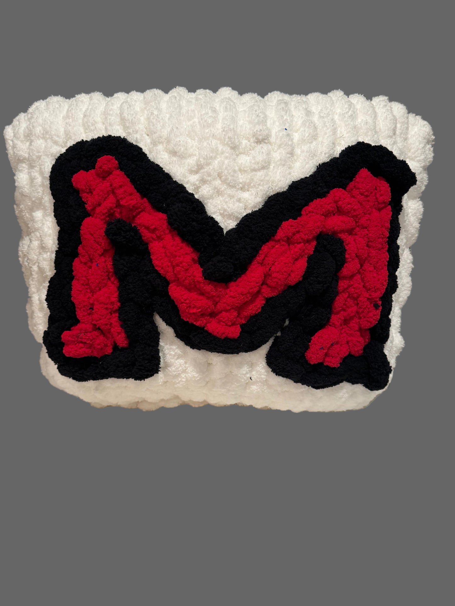 Crocheted letter 'M' in red and black on a white background