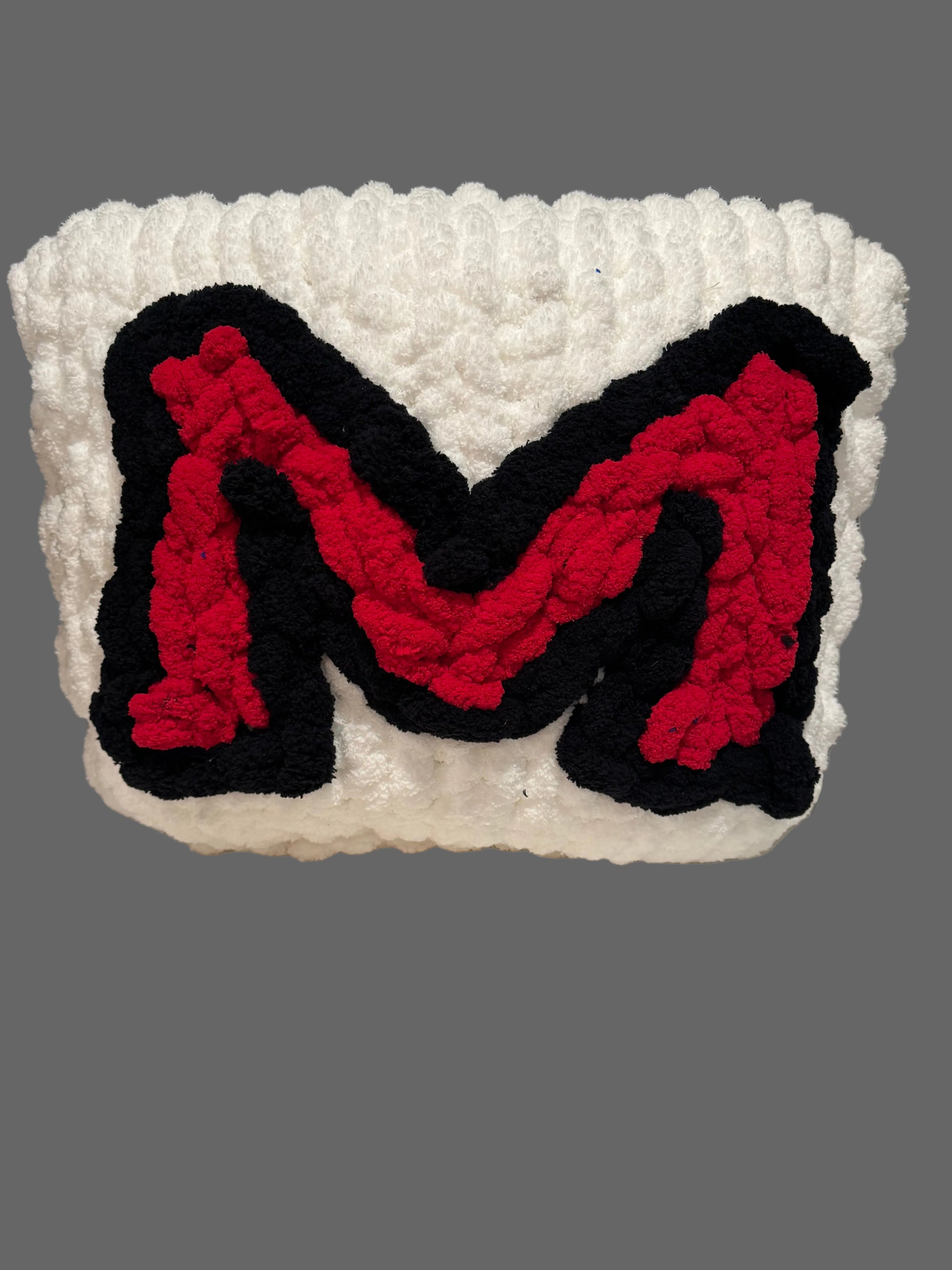 Crocheted letter 'M' in red and black on a white background