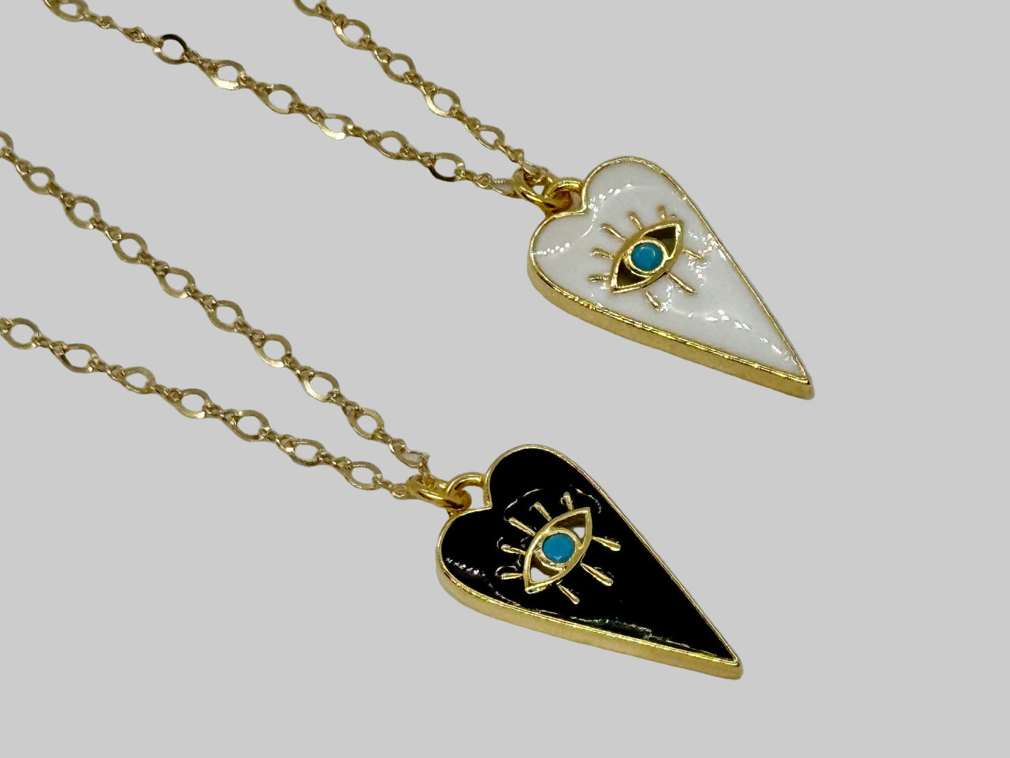 Two heart-shaped pendants on gold chains with eye designs and blue gemstones against a white background.
