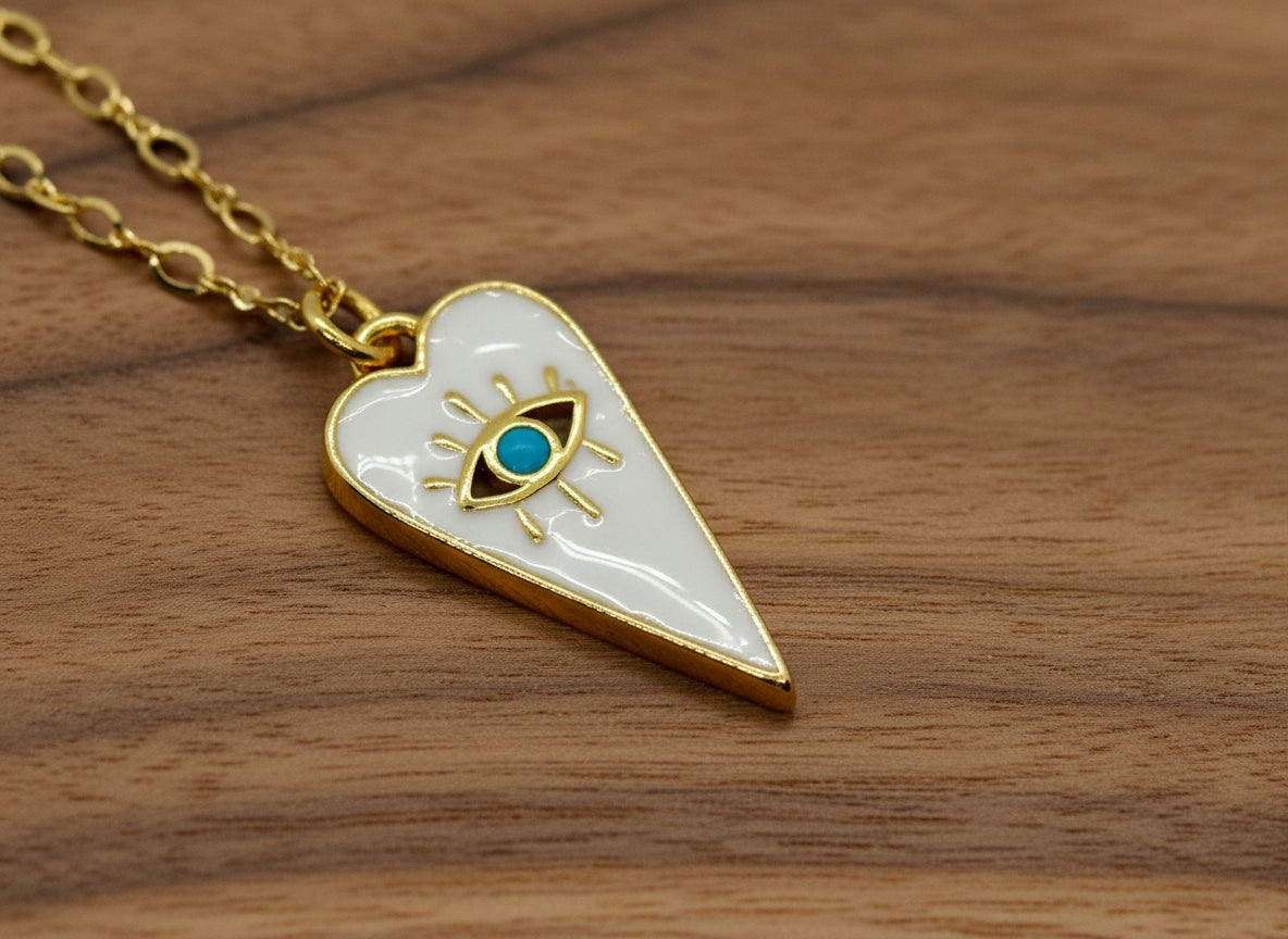 Heart-shaped pendant with eye design and gold chain on a light gray background
